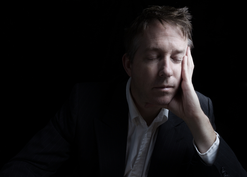 Portrait of businessman closing eyes while working late at night on black background with copy space